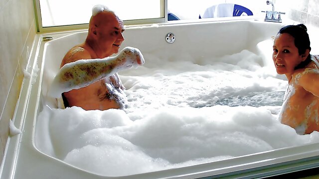 Slovakian woman and older man share a foamy nude bath in sunlit bathroom