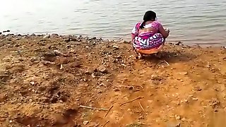 Indian woman peeing in the dirt by a lake