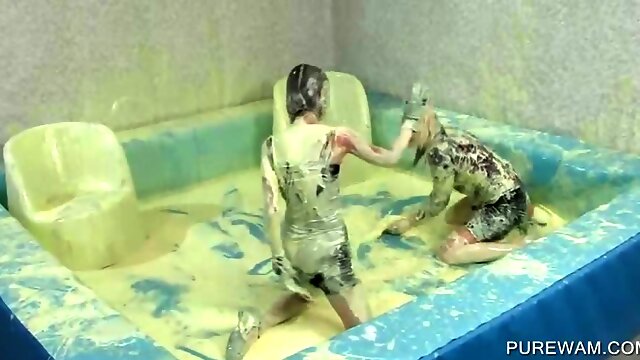 Clothed lesbos have fun in a pool of messy paint