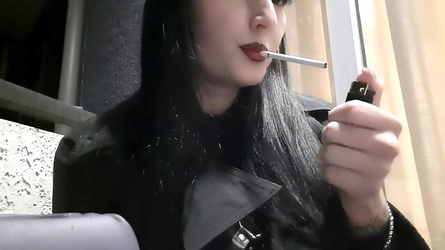 Dominatrix Nika smokes a cigarette on the balcony. Mistress sexy red lips blow smoke in your face