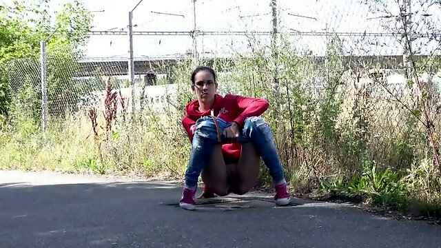 Cute nerdy brunette in sweatshirt and sneakers pisses on the road